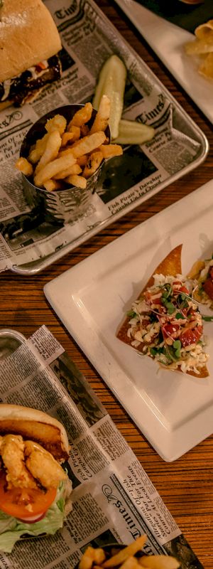 This image shows a variety of dishes including a sandwich, fries, nachos, a burger, a hot dog, and a salad on a wooden table.