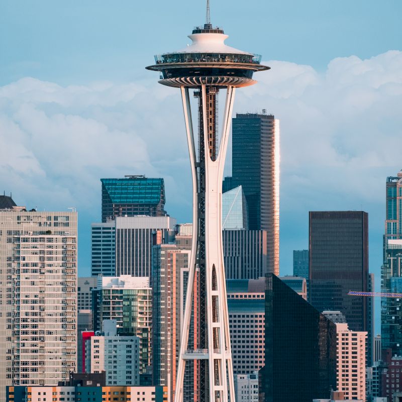The image features the Space Needle towering over the cityscape of Seattle, with a backdrop of various buildings and a partly cloudy sky.