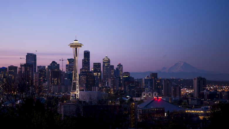 The image shows the Seattle skyline at dusk with the iconic Space Needle prominently featured and Mount Rainier visible in the background.