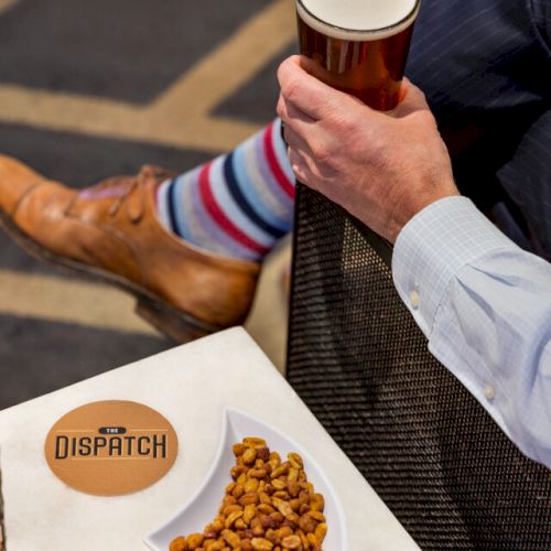 Person in striped socks and leather shoes holding a drink, with nuts and a candle on the table labeled 