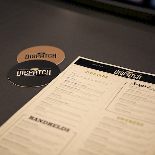 The image shows a restaurant menu on a table, accompanied by two coasters with the logo 