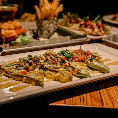 A variety of dishes on a table include a main entree with sauce, garnished with herbs, and a side of fries and sauce in the background.