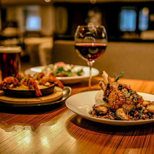 The image shows a table with a plated dish, skewered shrimp, and drinks including a glass of red wine in a restaurant setting.