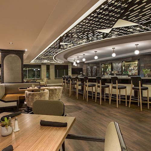 A modern restaurant interior with a stylish bar, various seating options including booths and tables, and a unique ceiling design.