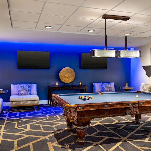 A stylish game room featuring a pool table, cozy seating, modern decor, and a wall with a Texas-shaped cutout and two mounted TVs.