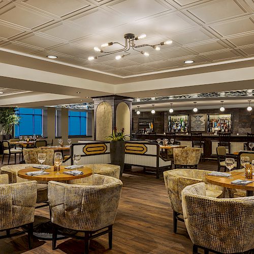 This image shows a modern, well-lit restaurant with several tables and chairs, elegant decor, and a bar area in the background.